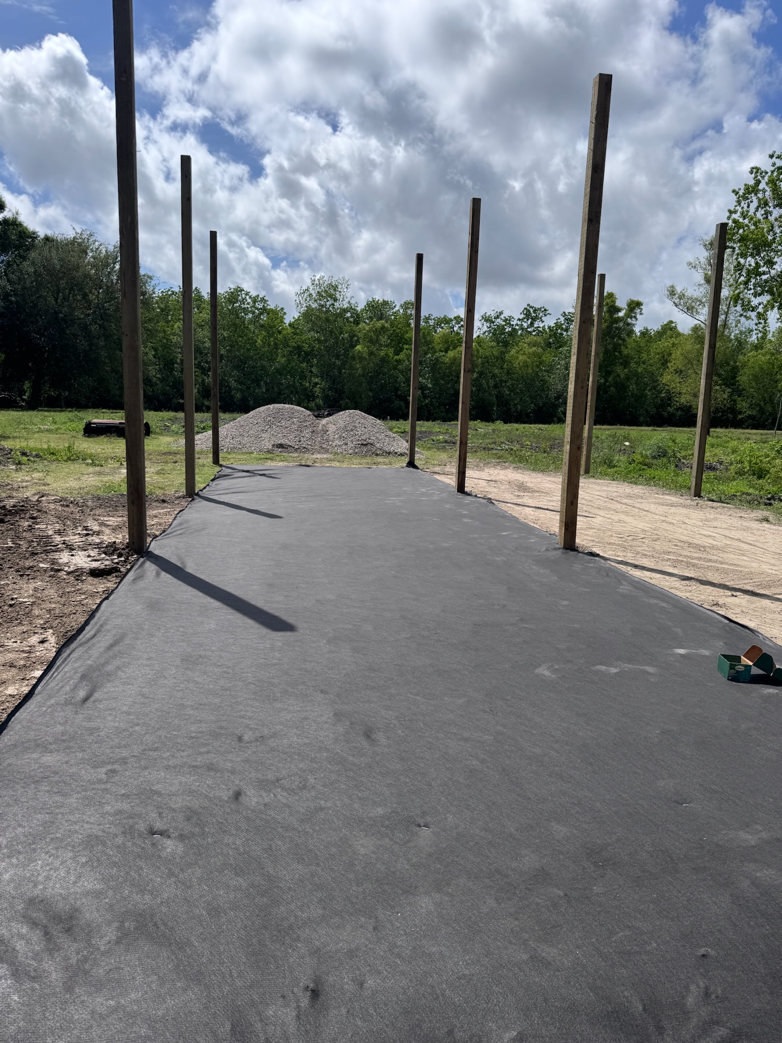 Geotextile fabric and posts on a cleared shop pad with a gravel pile waiting to spread