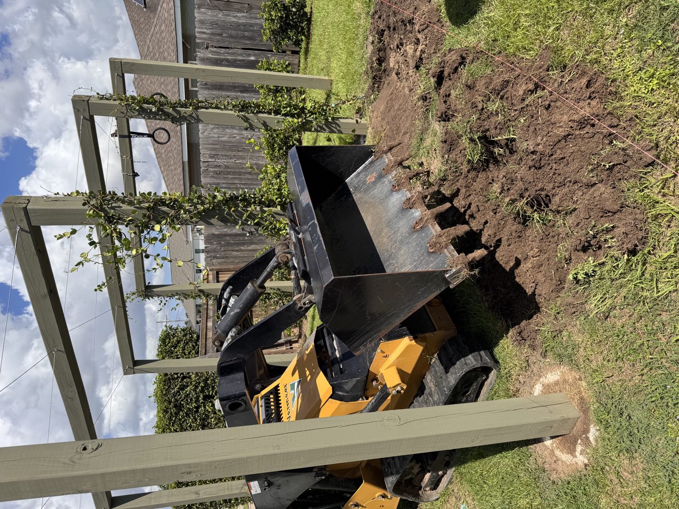 Compact track loader moving soil in a tight backyard under a pergola