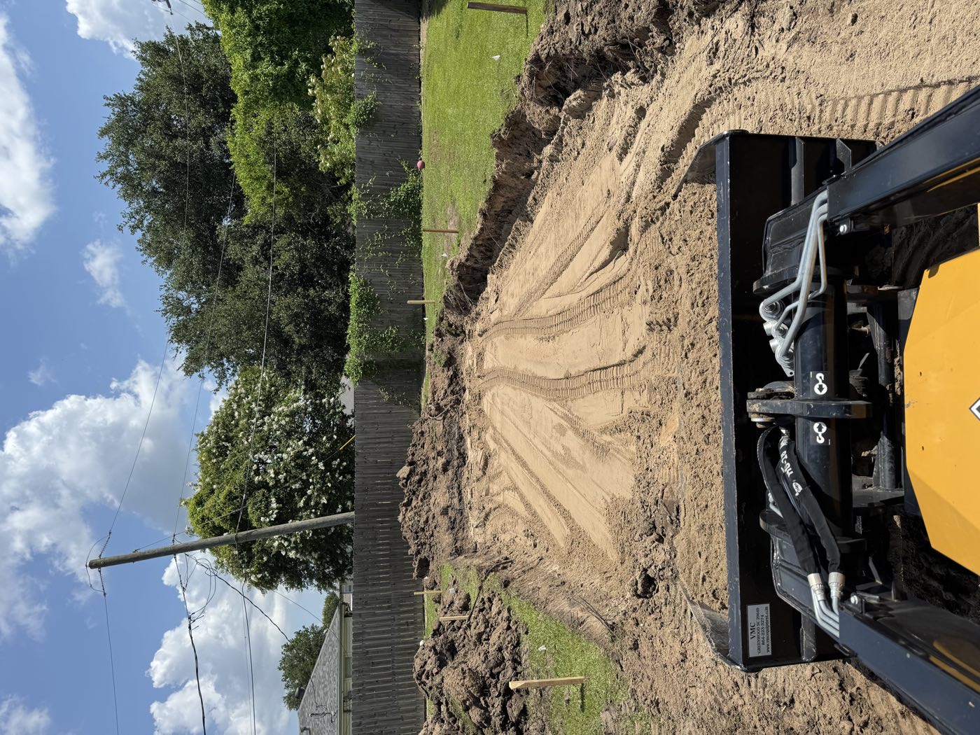 Track loader cutting and shaping a sand pad in a fenced backyard