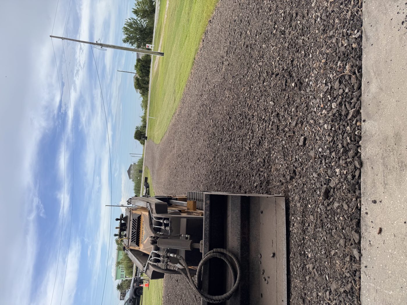 Track loader spreading dark gravel along a coastal driveway