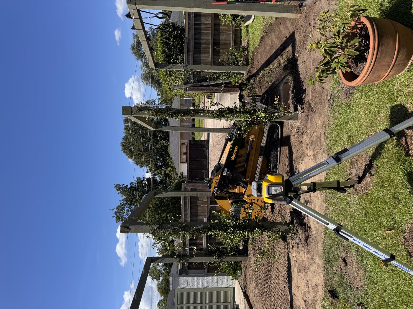 Laser level on a tripod while a Vermeer track loader grades a backyard