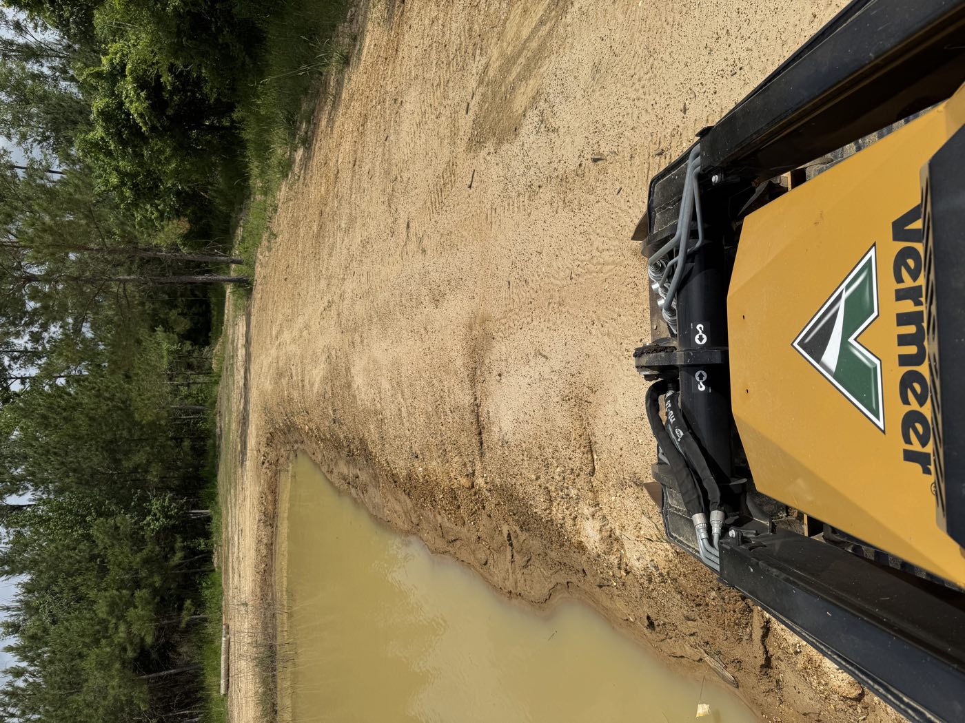 Operator view of a Vermeer building a sand berm along a pond