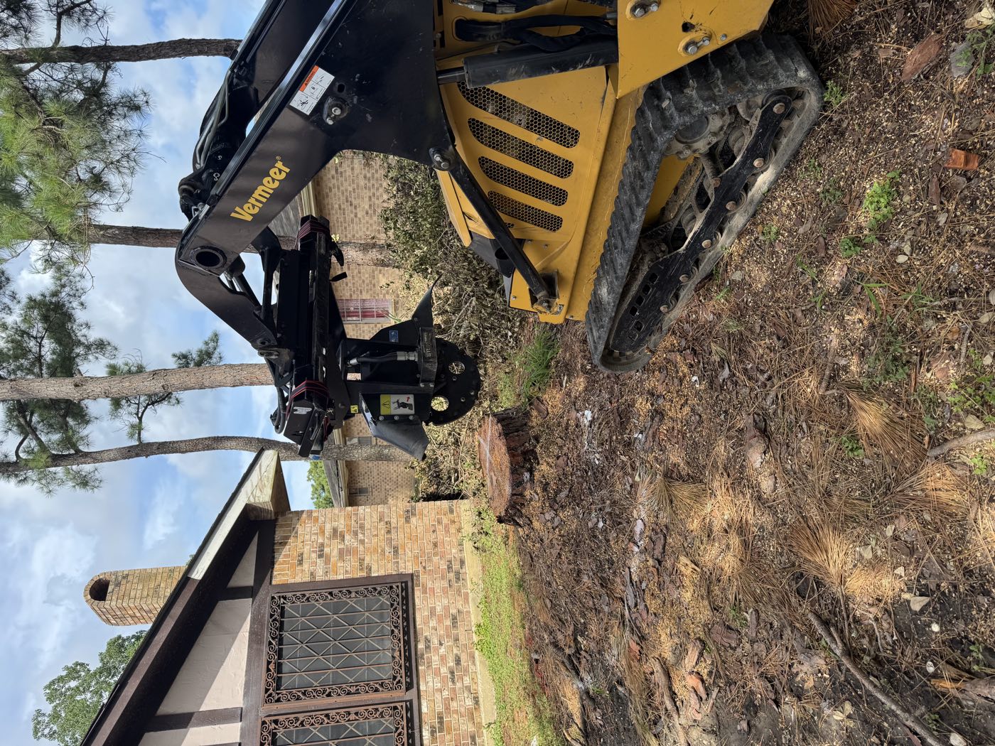 Vermeer track loader with a stump grinder attachment beside a residential stump